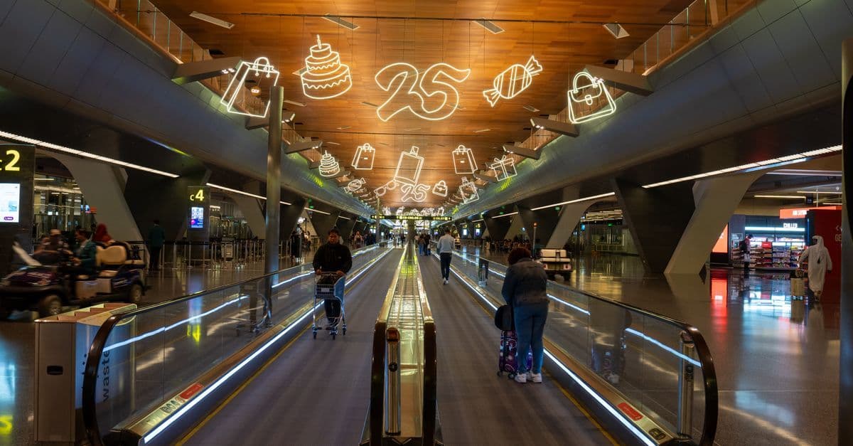 Reisende verlassen den Doha Flughafen durch die festlich dekorierte Halle in Richtung Stadtverbindungen.