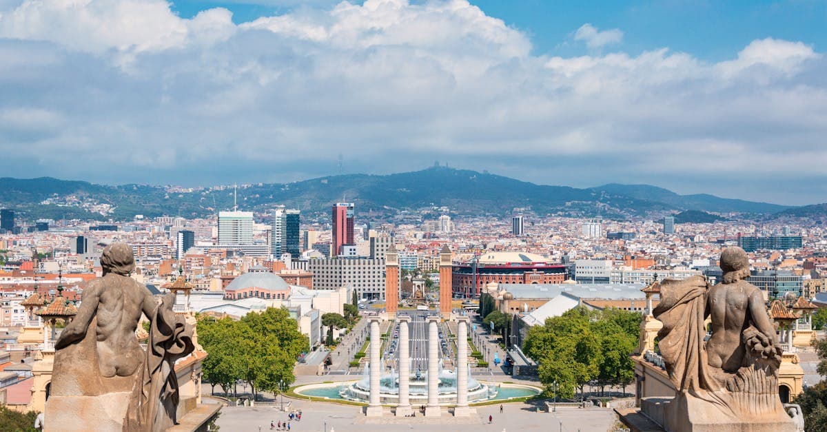 Uitzicht over Barcelona vanaf de Montjuïc-heuvel met standbeelden en een stralend blauwe lucht.