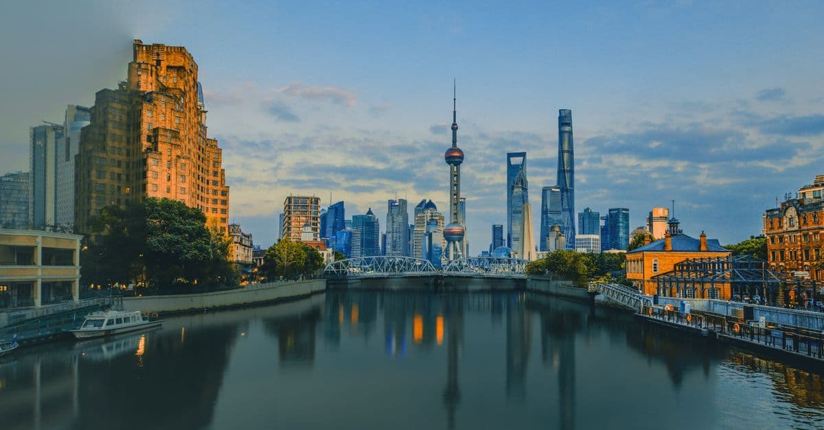 Shanghai's Pudong skyline rises above the river at dusk, with illuminated towers reflected in the water.