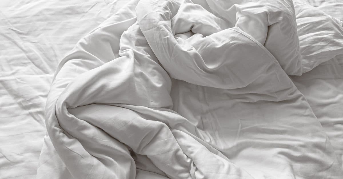 Verfrommeld wit dekbed zonder overtrek dat warmte en slaapcomfort uitstraalt in een minimalistische slaapkamer.