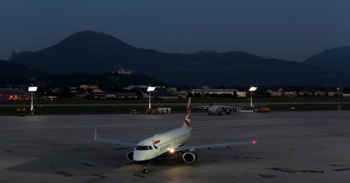 Flugzeug auf dem Vorfeld des Salzburg Airport bei Abenddämmerung mit beeindruckender Bergsilhouette im Hintergrund.