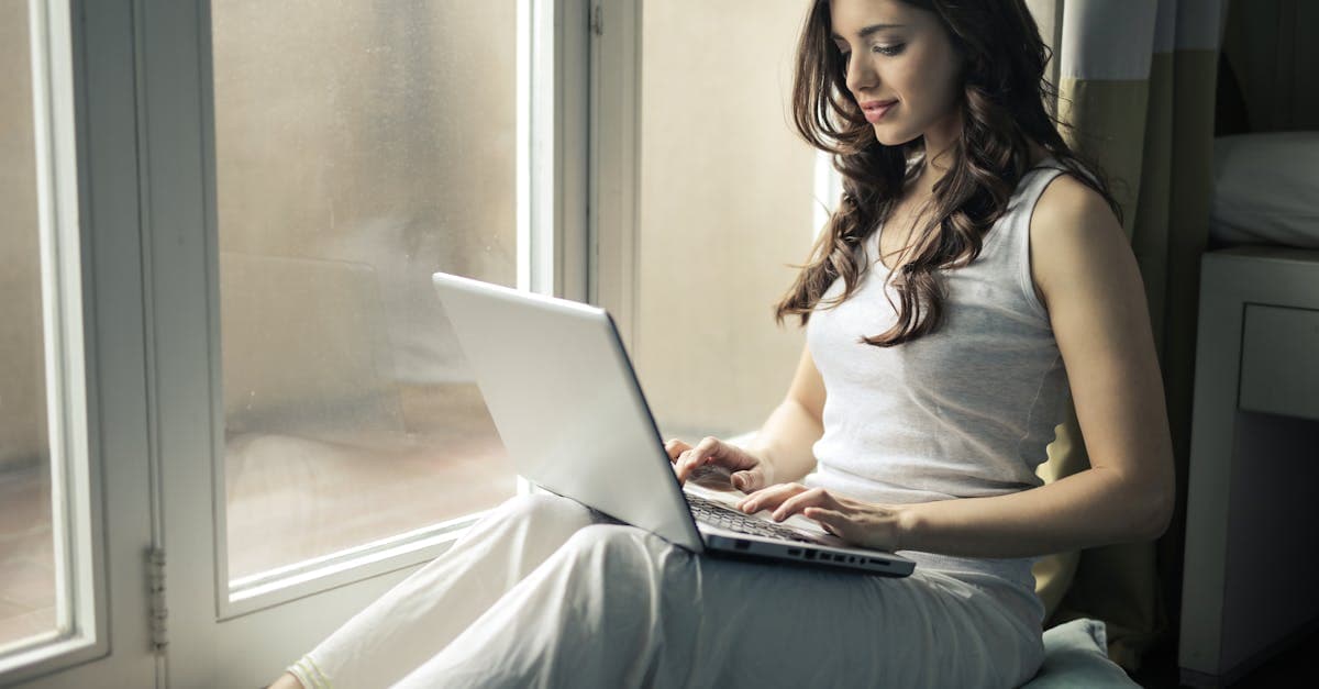 Woman working remotely on a laptop by a bright window, staying connected while living in Ireland.