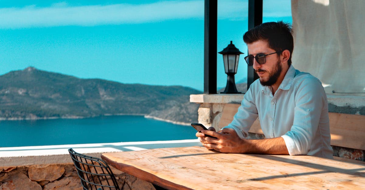 Antalya'da dağ manzaralı kafede oturan adam, roaming ne demek diye araştırırken telefonunu kullanıyor