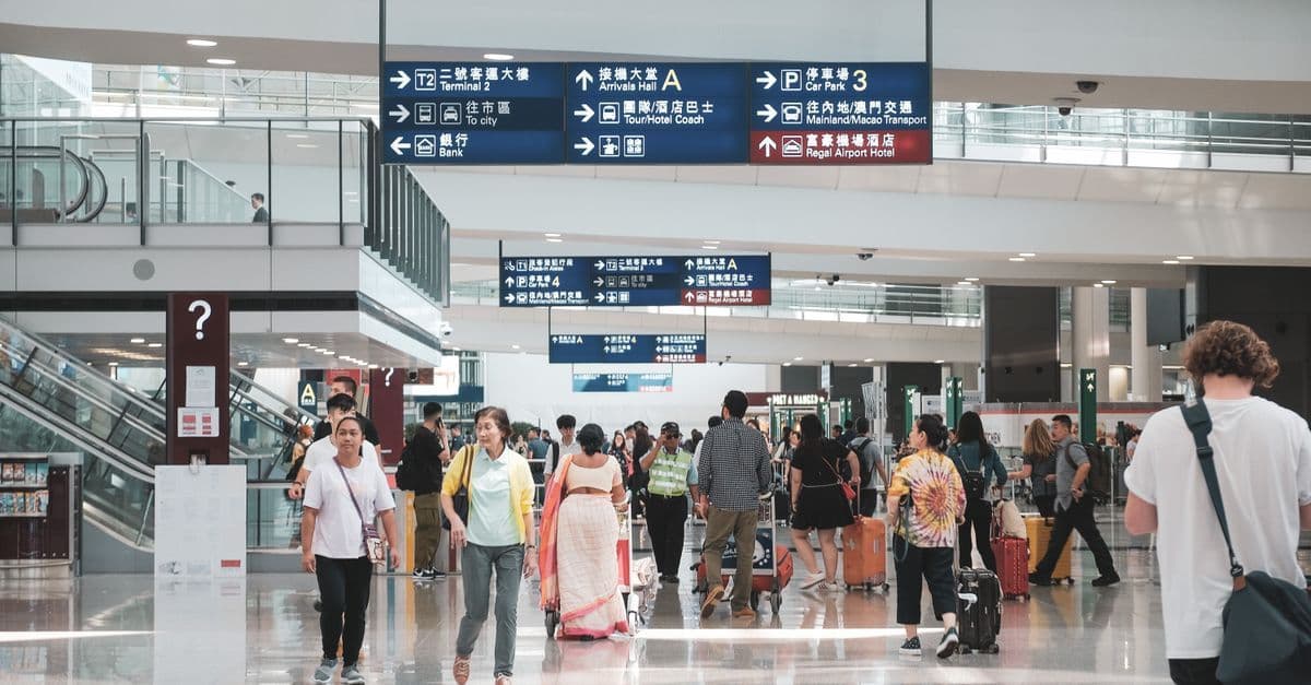 Busy airport terminal with diverse travellers arriving for International Hall student accommodation check-in.