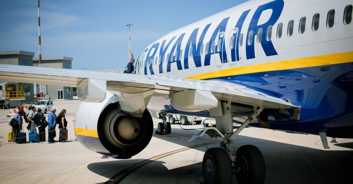 Passeggeri in fila per imbarcarsi su un aereo Ryanair in una giornata di sole.