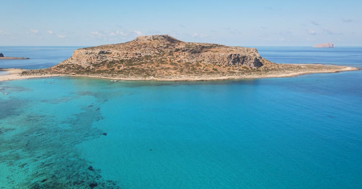 Flygfoto över en avlägsen grekisk ö omgiven av kristallklart turkost vatten under klarblå himmel.