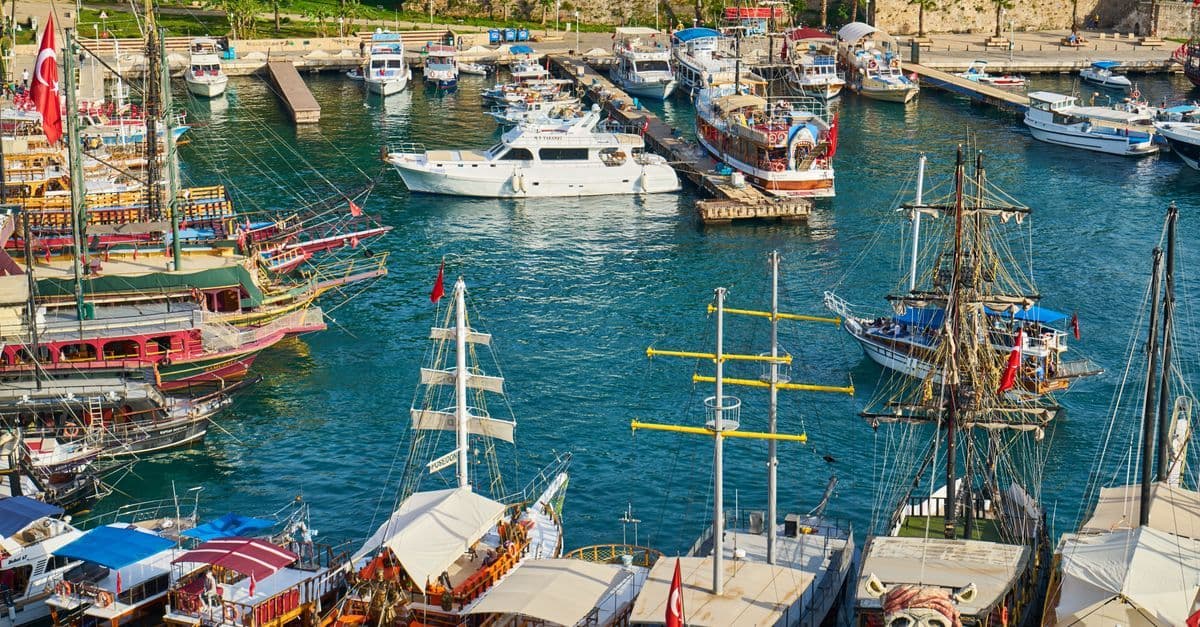Ausflugsboote und Segelschiffe liegen im Hafen von Antalya, an mehreren Masten wehen türkische Flaggen.