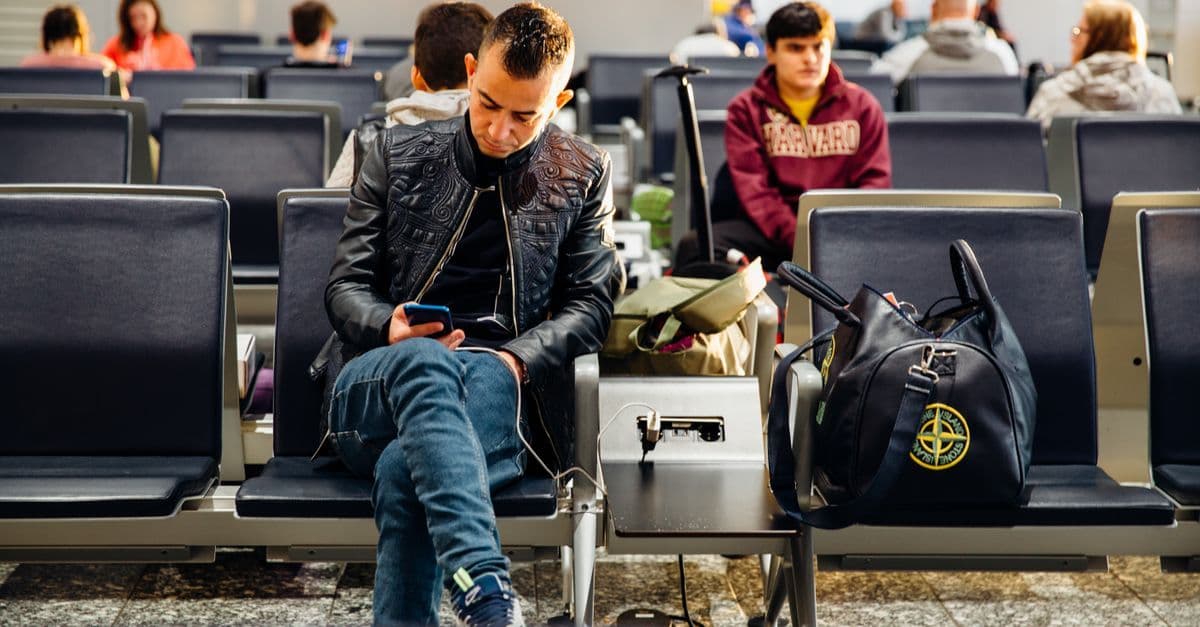 Pasajeros en sala de espera de aeropuerto consultando sus teléfonos para saber que es esim