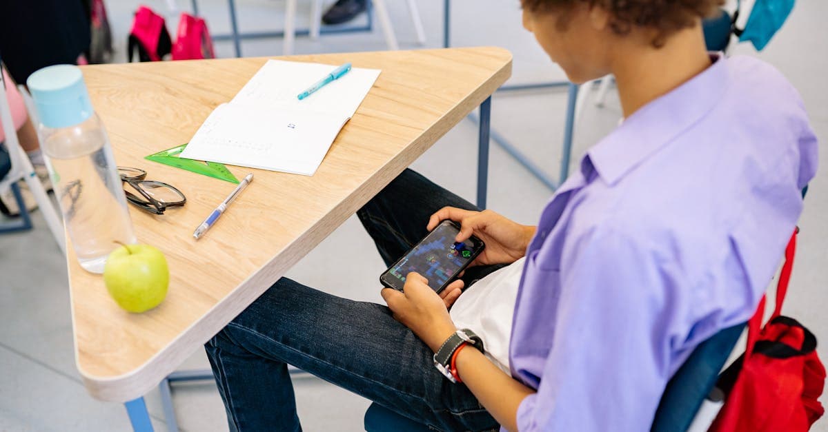 Child engaging with a mobile game on a smartphone at a school desk with supplies nearby