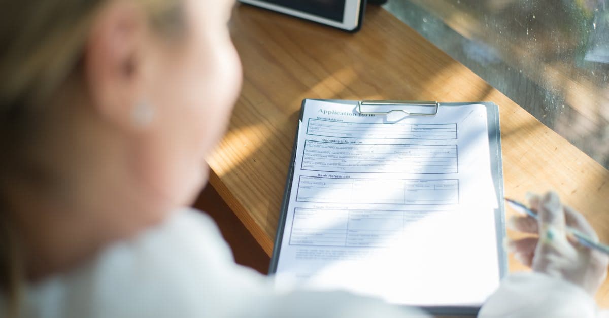 Woman filling out a UK passport renewal application form by hand at a sunlit wooden desk
