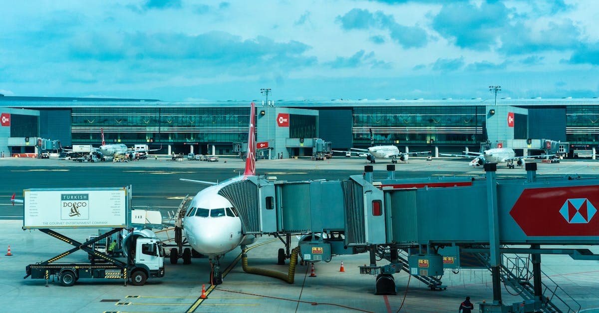 Flygplan vid gate med jetway och servicevagnar på ett vältrafikerat flygfält.