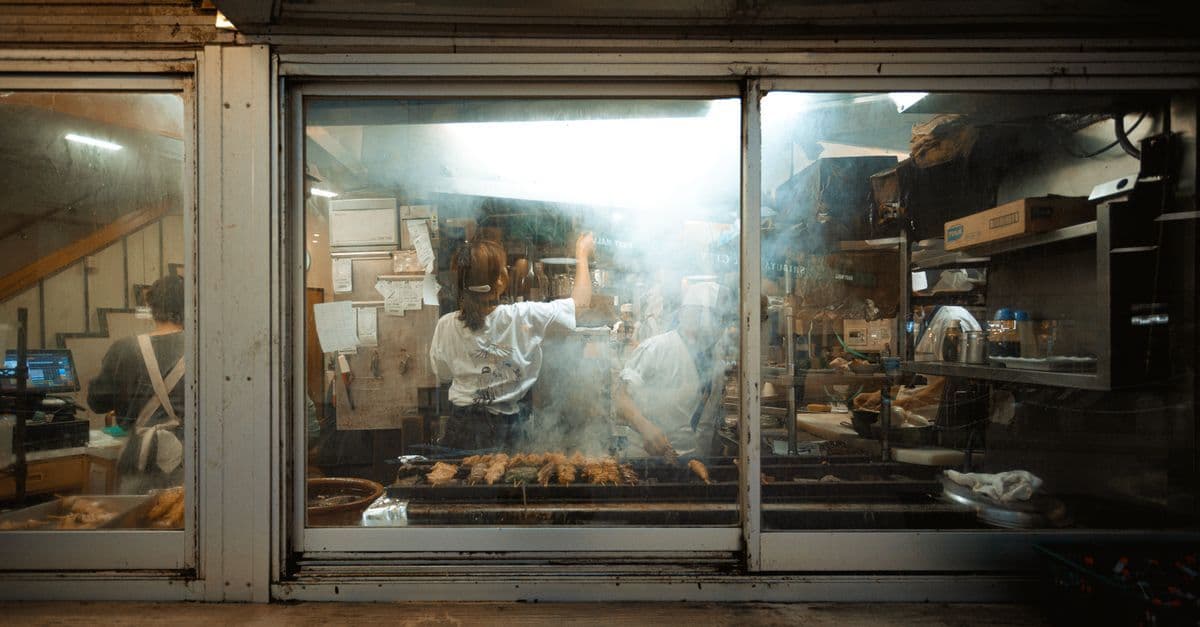 Chefs grilling skewers over open flames in a smoky tokyo grill kitchen