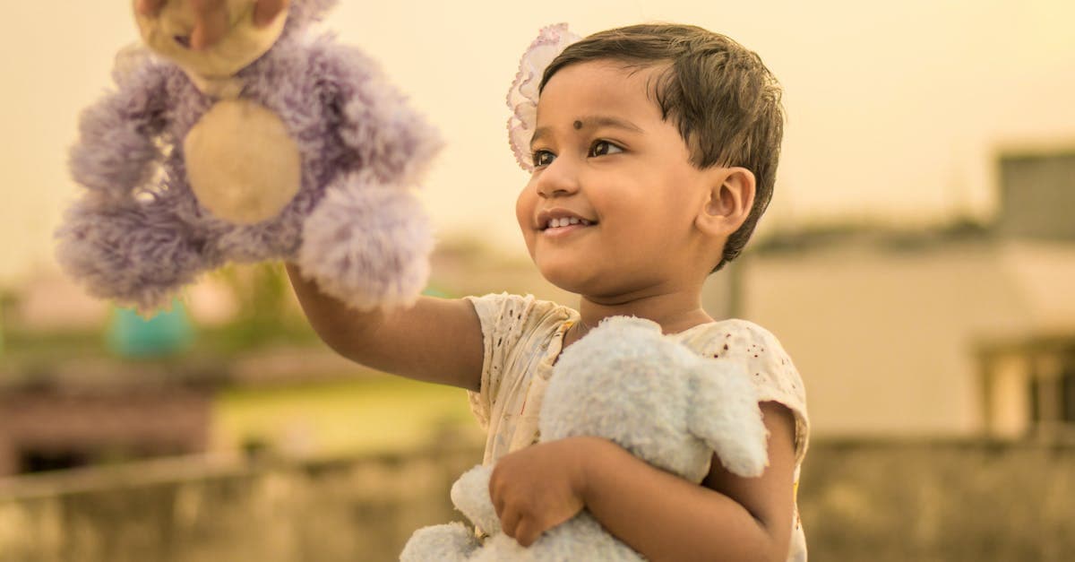 Niño sonriente jugando felizmente con su perrito Fisher Price y otros juguetes de peluche al aire libre.