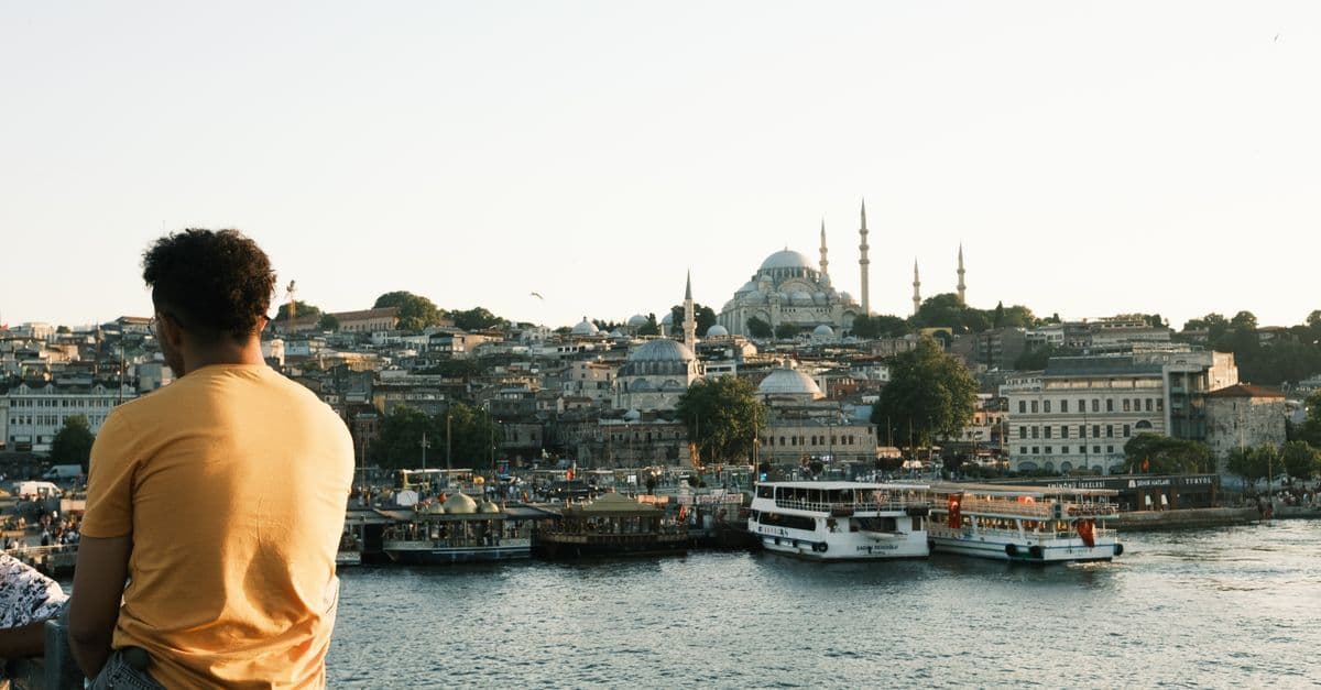 Un uomo osserva i traghetti a Istanbul, con la moschea di Solimano e gli edifici della città sullo sfondo.
