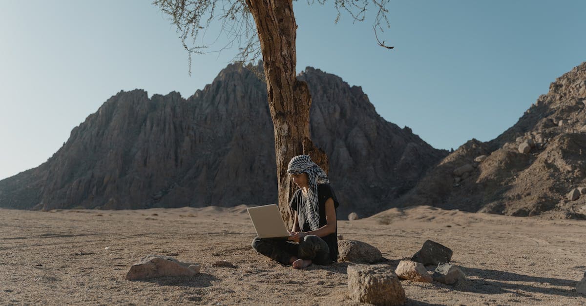 Perempuan bekerja dengan laptop di bawah pohon di gurun berbatu memahami legalitas kerja remote luar negeri