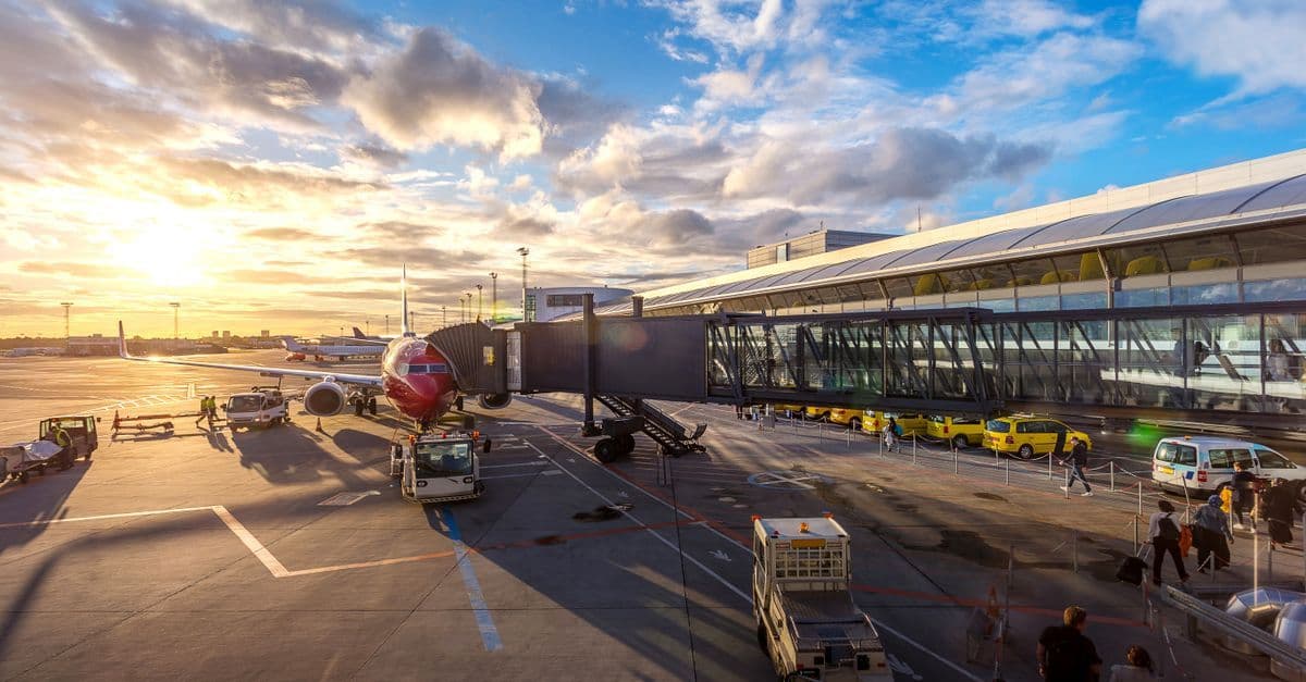 Rejsende tjekker ind tidligt i Billund Lufthavn med udsigt over startbanen i solnedgangen.