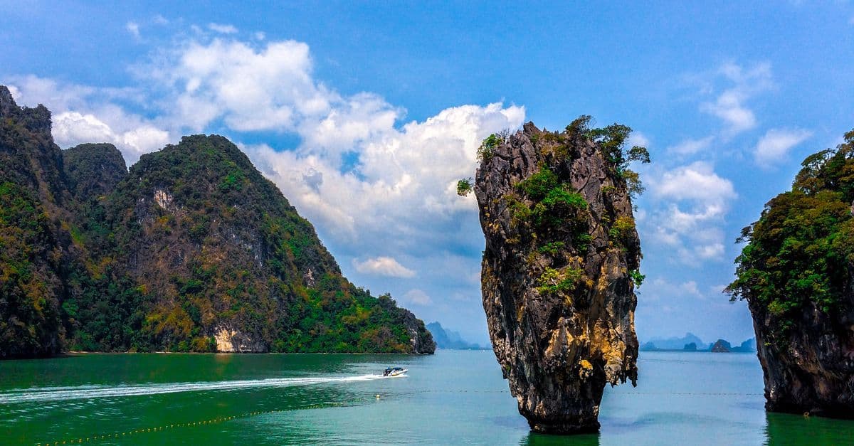 A tall limestone sea stack rises from the water among forested islands in Phang Nga Bay near Phuket.