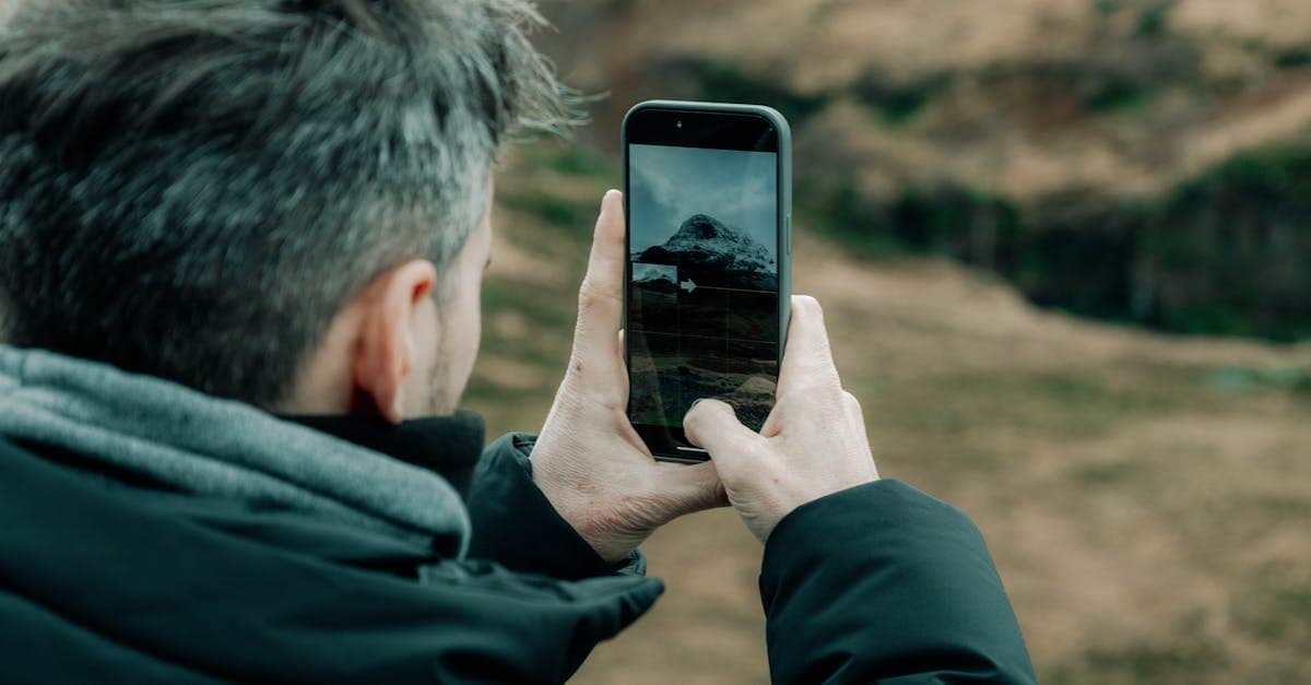 Photographer using a phone to capture a stunning mountain view outdoors near Edinburgh, Scotland.