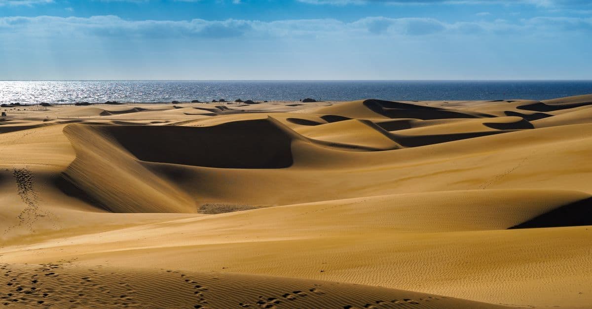 Gyllene sanddyner möter havet under klarblå himmel i Gran Canaria, format av calima och passatvindarna.