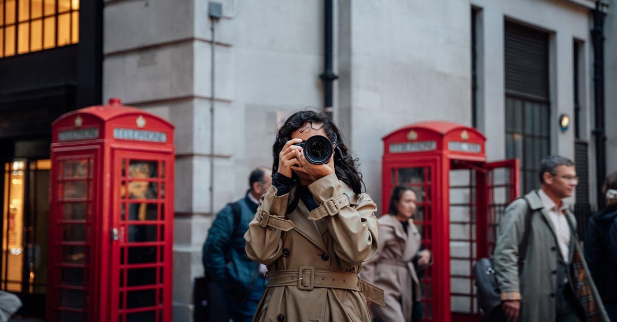 Woman photographing on a busy London street, with traditional red phone boxes visible in the background.