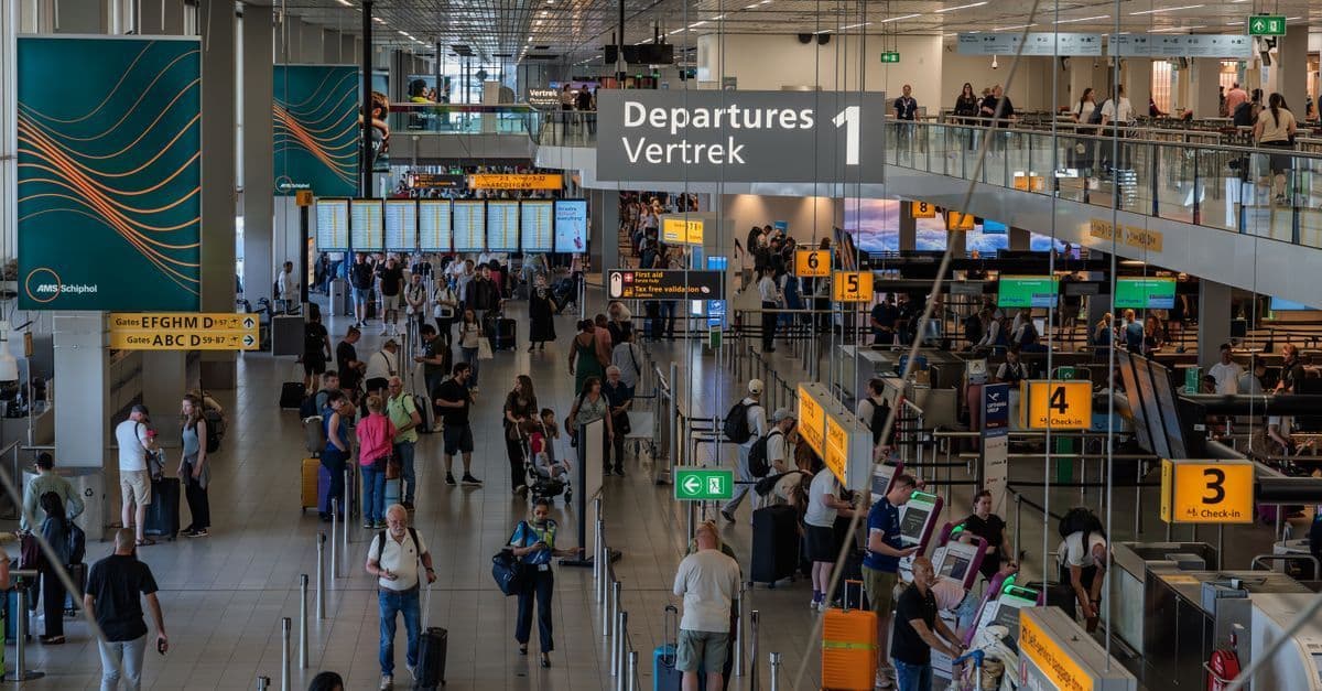 Drukke vertrekhal van Amsterdam Airport Schiphol met reizigers op weg naar hun gate.