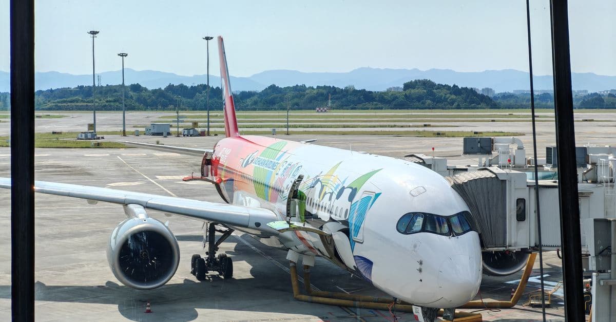 Brightly coloured passenger aircraft parked at an airport gate with a dramatic mountain range in the background.