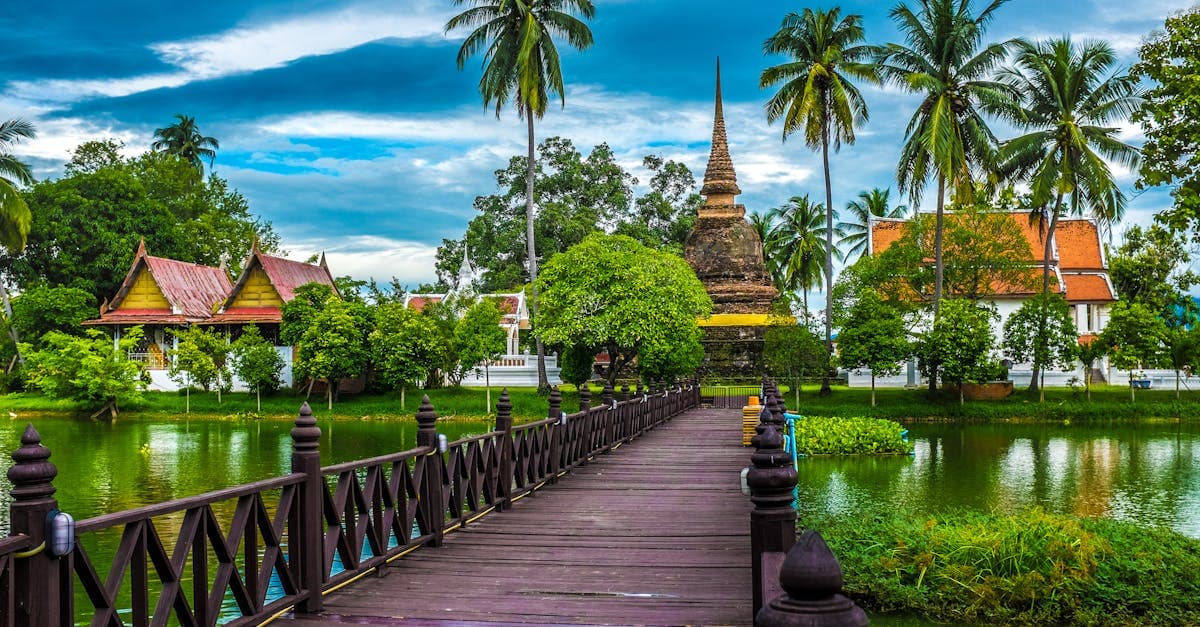 Buddhistischer Tempel von Sukhothai inmitten grüner Natur und spiegelndem Wasser, typisch für das Thailand Wetter im Landesinneren.