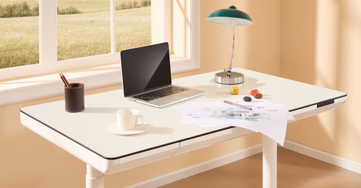 A bright modern home office with an adjustable desk, laptop, desk lamp, and design sketches by the window.