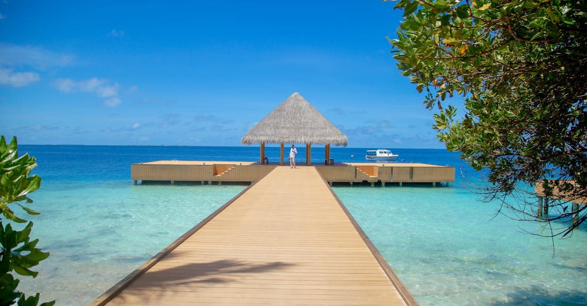 Wooden jetty extending over a turquoise lagoon to a thatched overwater bungalow on maldives holidays