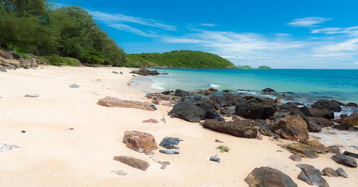 Turquoise waters and lush rocks on a peaceful Thai beach during the dry season from November to April.