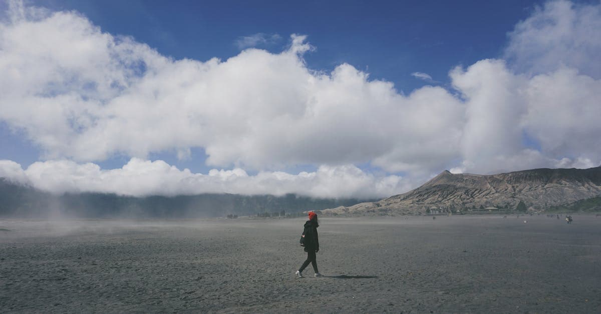 Seorang pejalan kaki menyusuri dataran abu vulkanik Gunung Bromo, mempertimbangkan biaya premi asuransi perjalanan.