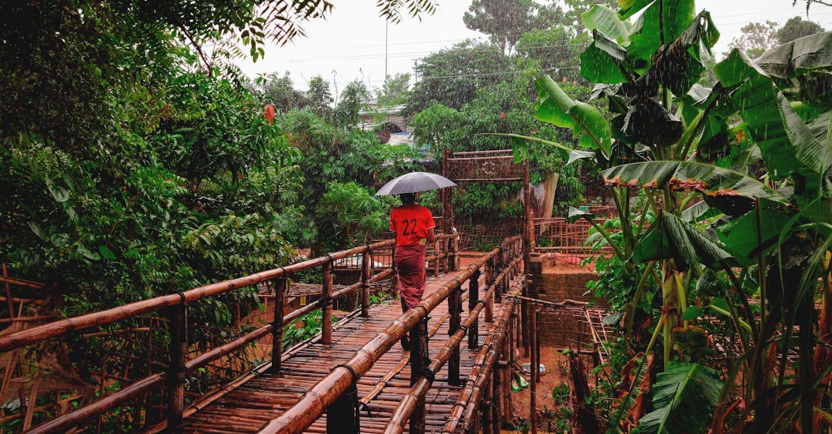 Hombre bajo lluvia torrencial en un puente de bambú, mostrando el tiempo en Bali en su mes más lluvioso