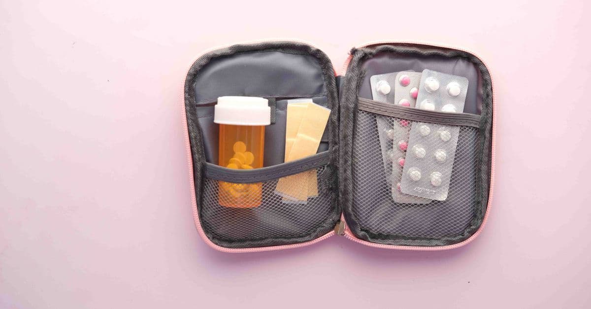Ein geöffnetes Reiseetui enthält eine Tablettenflasche, Pflaster und Blisterpackungen als kompakte Reiseapotheke.