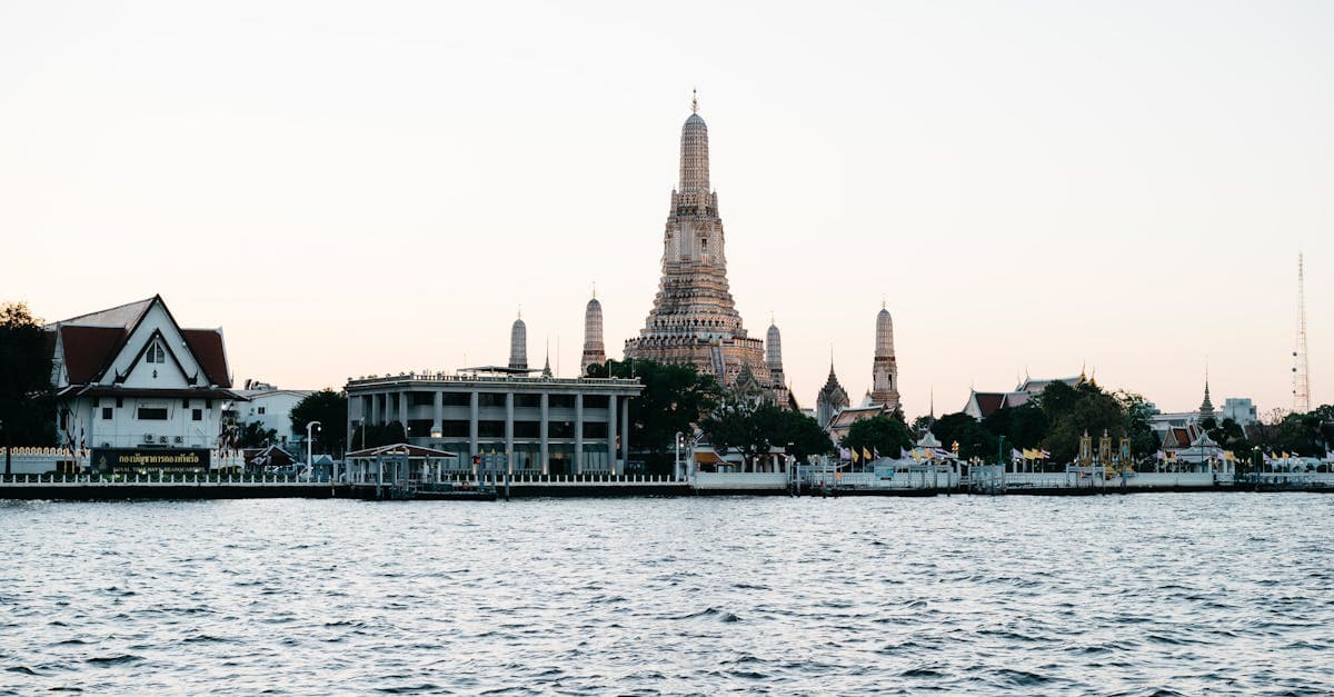 Wat Arun temple glowing beside Bangkok's Chao Phraya River at dusk, a budget-friendly place to visit in Thailand