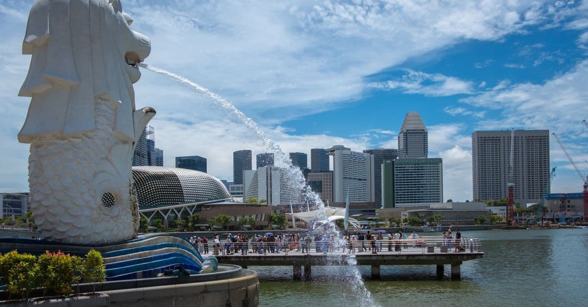 รูปปั้นเมอร์ไลออนพ่นน้ำตัดกับสกายไลน์สิงคโปร์และ Marina Bay อันงดงามในวันแดดจ้า