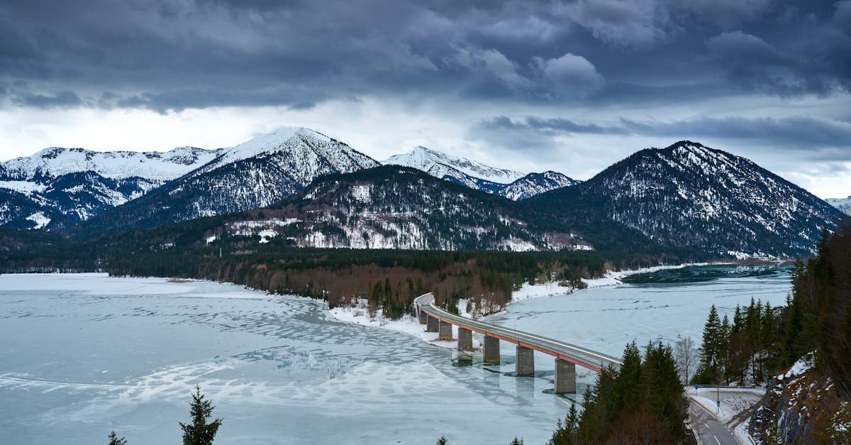 Stunning winter view of bridge over frozen lake and snowy Bavarian Alps in Lenggries, Germany.