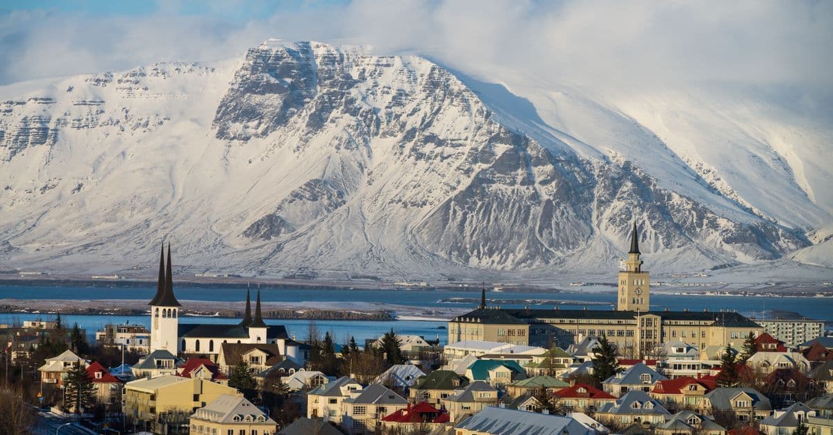 Casas de colores y una iglesia frente a un fiordo y montañas nevadas bajo el sol de invierno en Islandia.