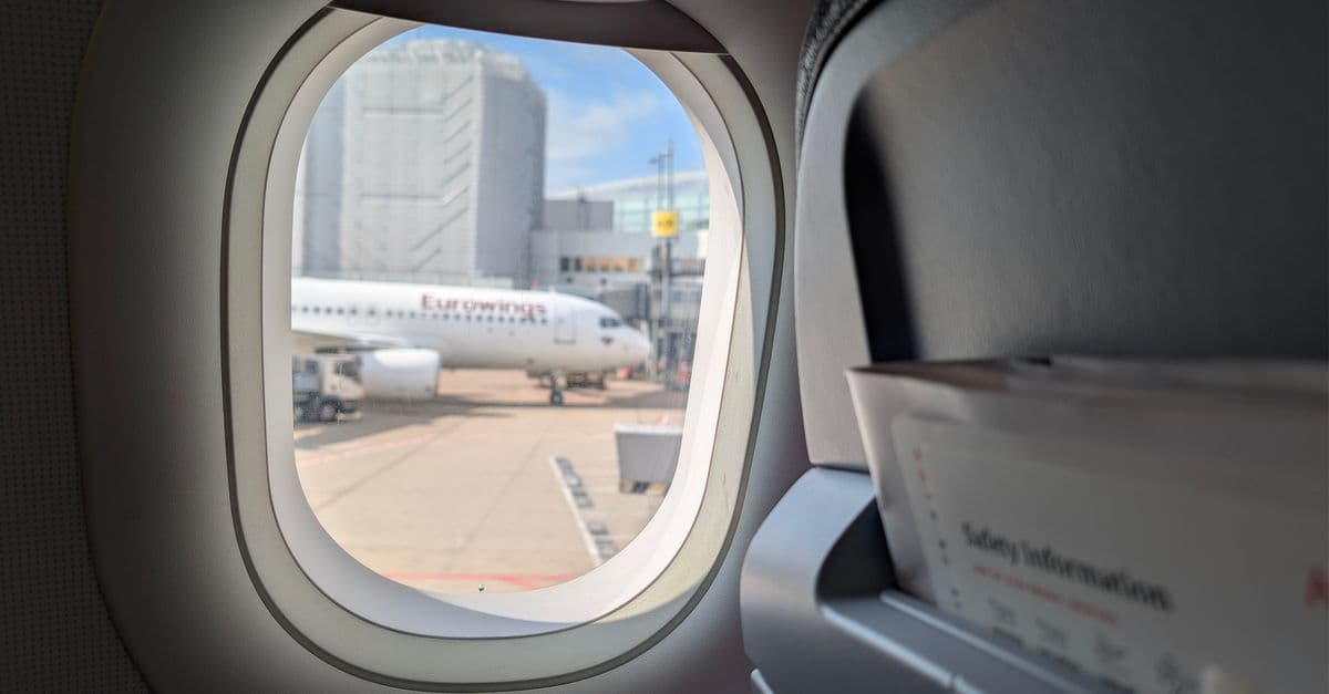 Blick aus dem Flugzeugfenster auf das Rollfeld des Düsseldorfer Flughafens mit einem Eurowings-Flugzeug im Hintergrund.