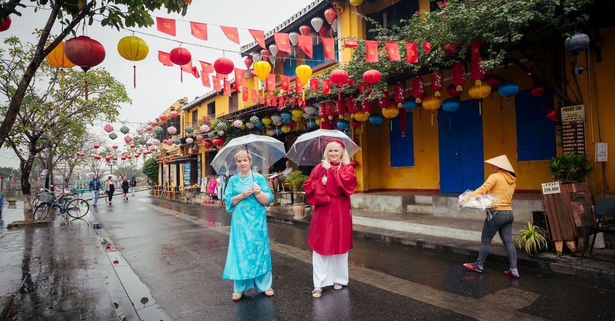 燈籠高掛的老街雨後路面濕亮,兩名遊客穿著雨衣、撐傘漫步,呈現越南雨天景象。