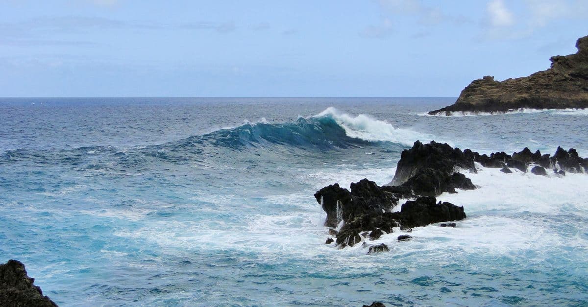 Waves break against jagged coastal rocks beneath a partly cloudy sky.