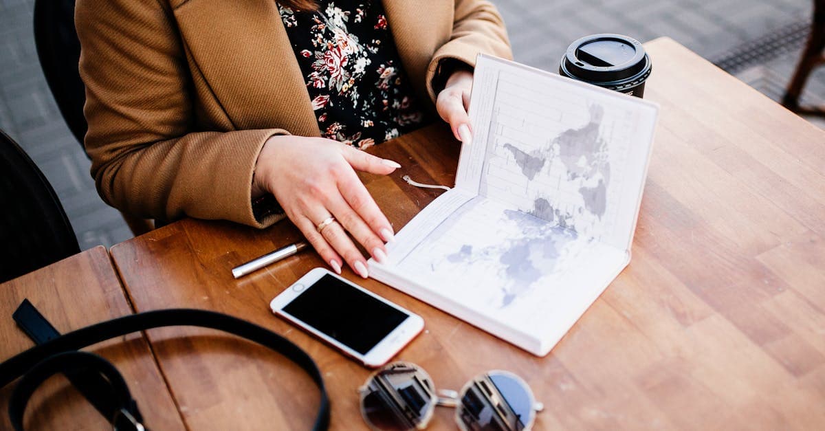 Mujer revisando un mapa y herramientas de travel planner junto a un café y un smartphone en mesa de madera.