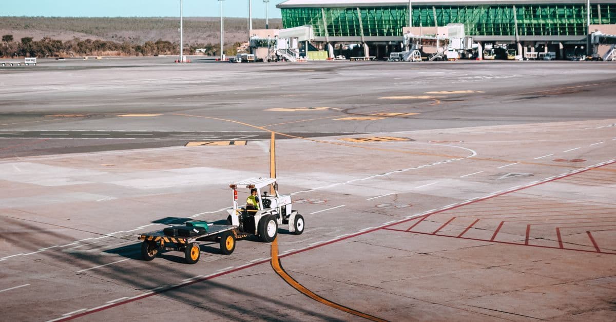 Sydney Airport international terminal building with luggage cart on the tarmac under blue skies.