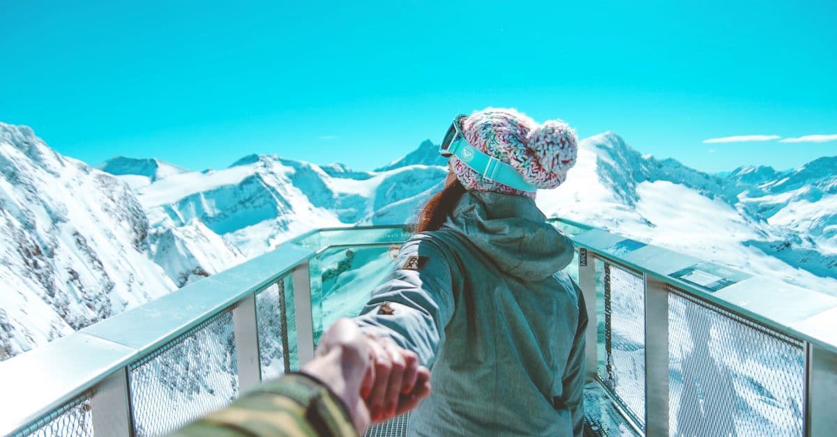 Frau in Winterkleidung hält Hand und spaziert auf verschneiter Aussichtsplattform in den Alpen