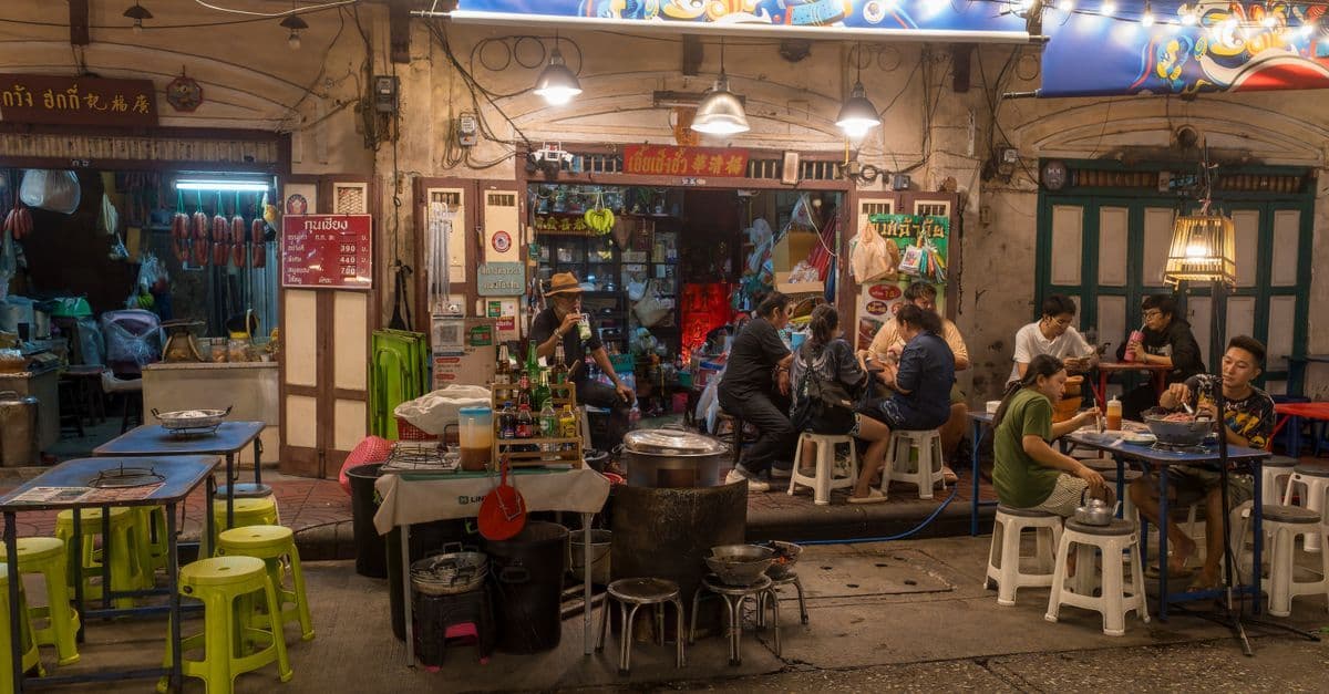 Abendliche Streetfood-Szene in Bangkoks Silom-Viertel mit Menschen beim Essen unter warmem Licht nach Feierabend.