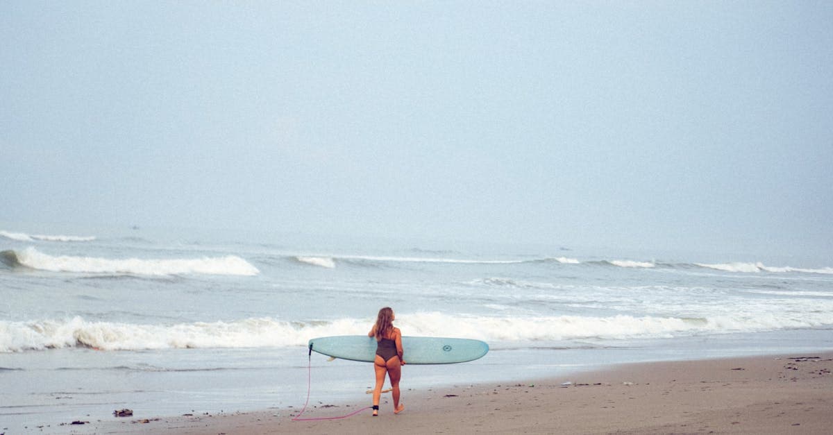 バリ旅行のビーチでサーフボードを抱えて波を見つめる女性観光客の姿