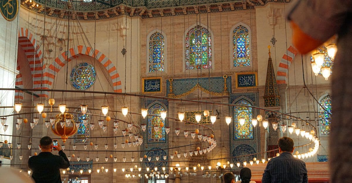 Besucher in einer Moschee in Istanbul, einer fotografiert mit dem Handy die bunten Glasfenster.