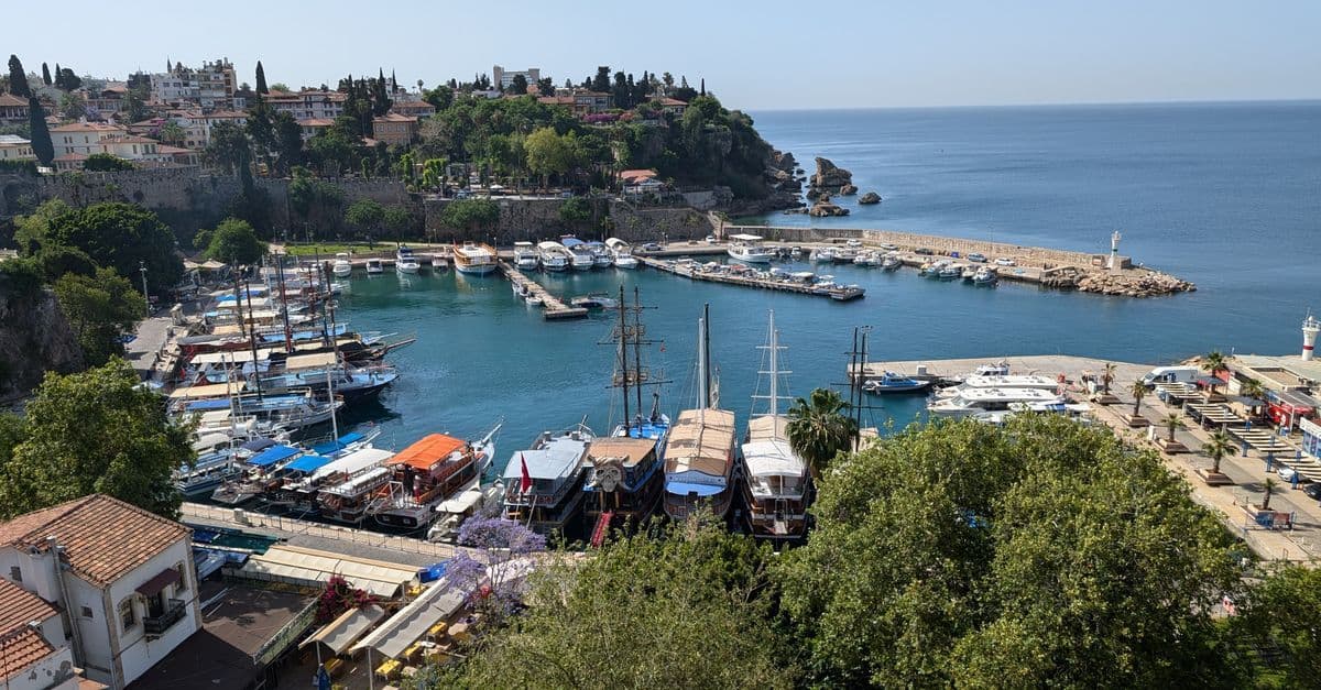 Båtar i den gamla hamnen i Antalya, nedanför gamla stadens murar och hus, med havet bakom piren.