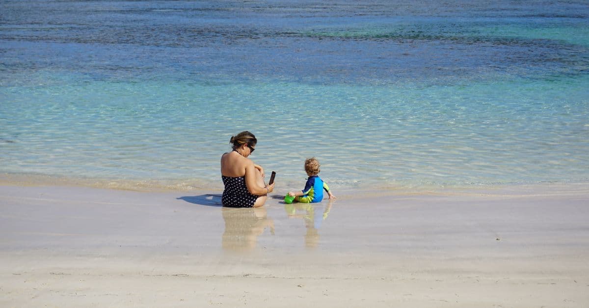 Eine Frau und ein Kind sitzen am flachen Ufer im klaren Wasser eines ruhigen Strandes.