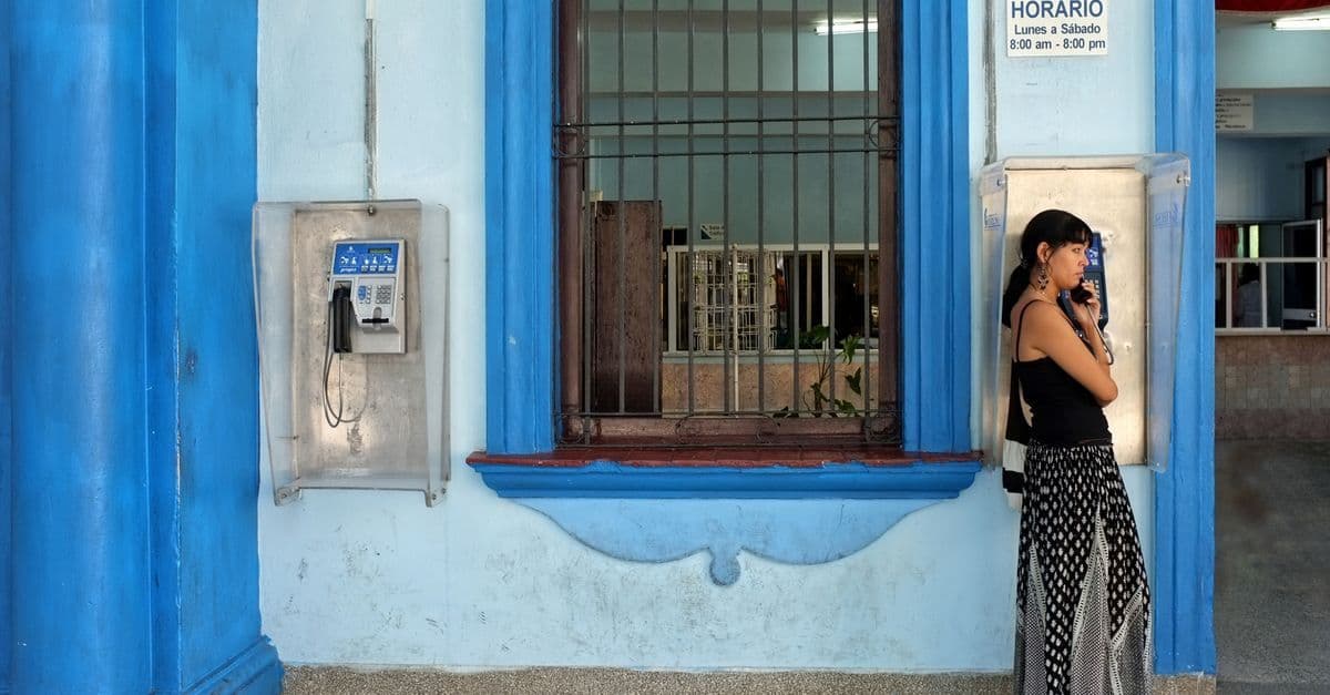 Jeune femme utilisant un téléphone public dans une rue bleue vibrante de Cuba pour rester connectée.