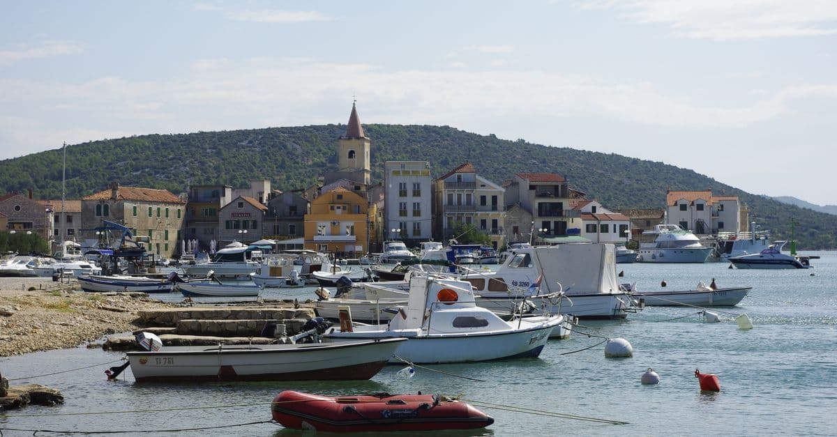 Boote im Hafen von Pirovac vor bunten Häusern und Hügeln – ideale Kulisse für einen Kroatien Urlaub.
